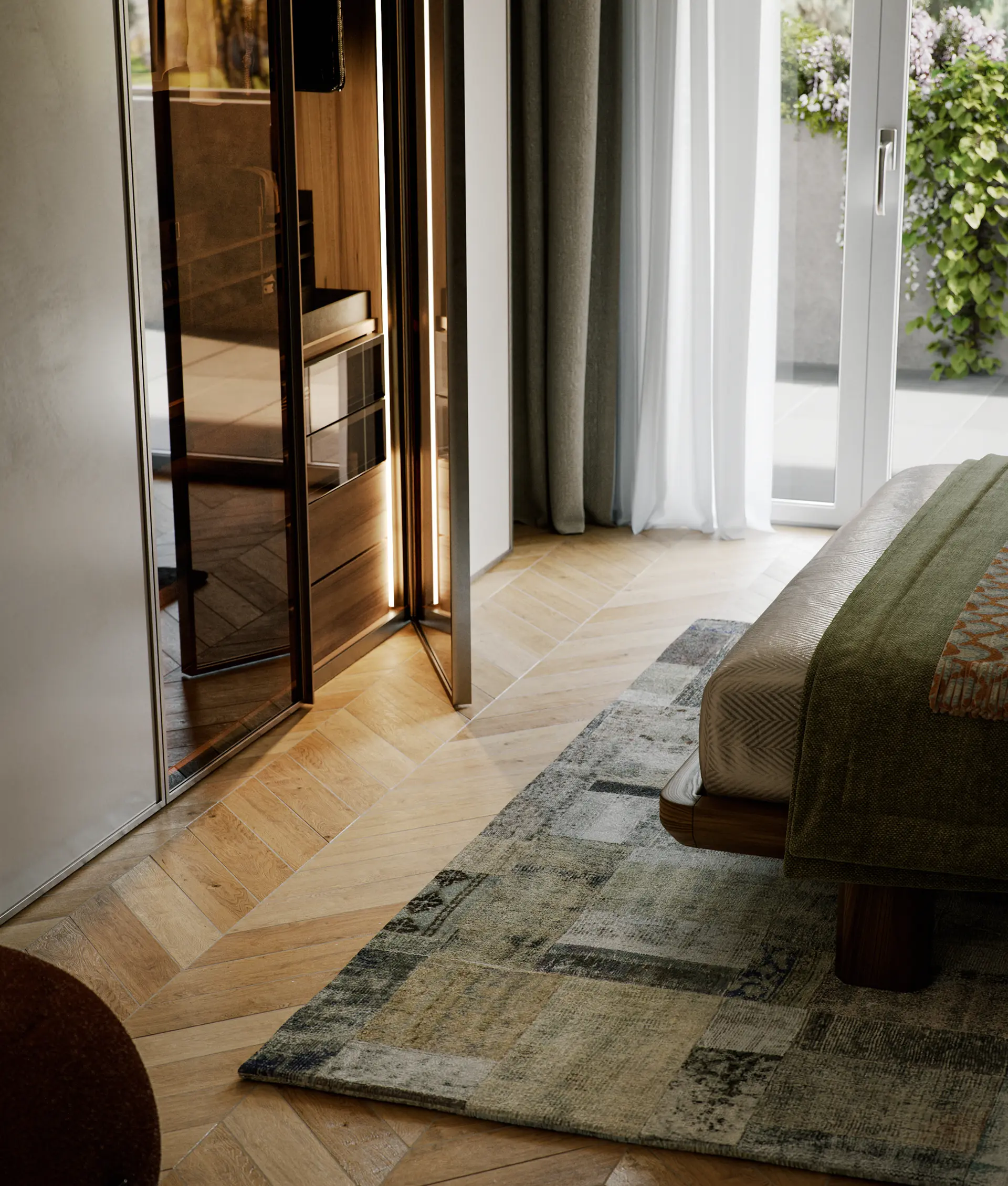 Bedroom corner with wooden floor, patterned rug, part of a bed with green blanket, and open mirrored closet door reflecting light.